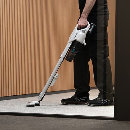 Person using a cordless vacuum cleaner on a floor with a wooden wall background