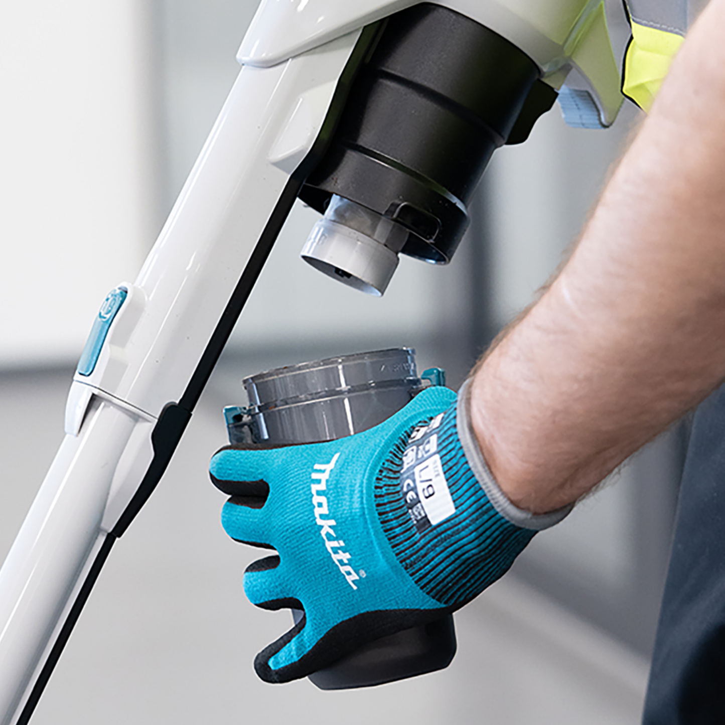 Person wearing a blue Makita glove using a power tool on a blurred background