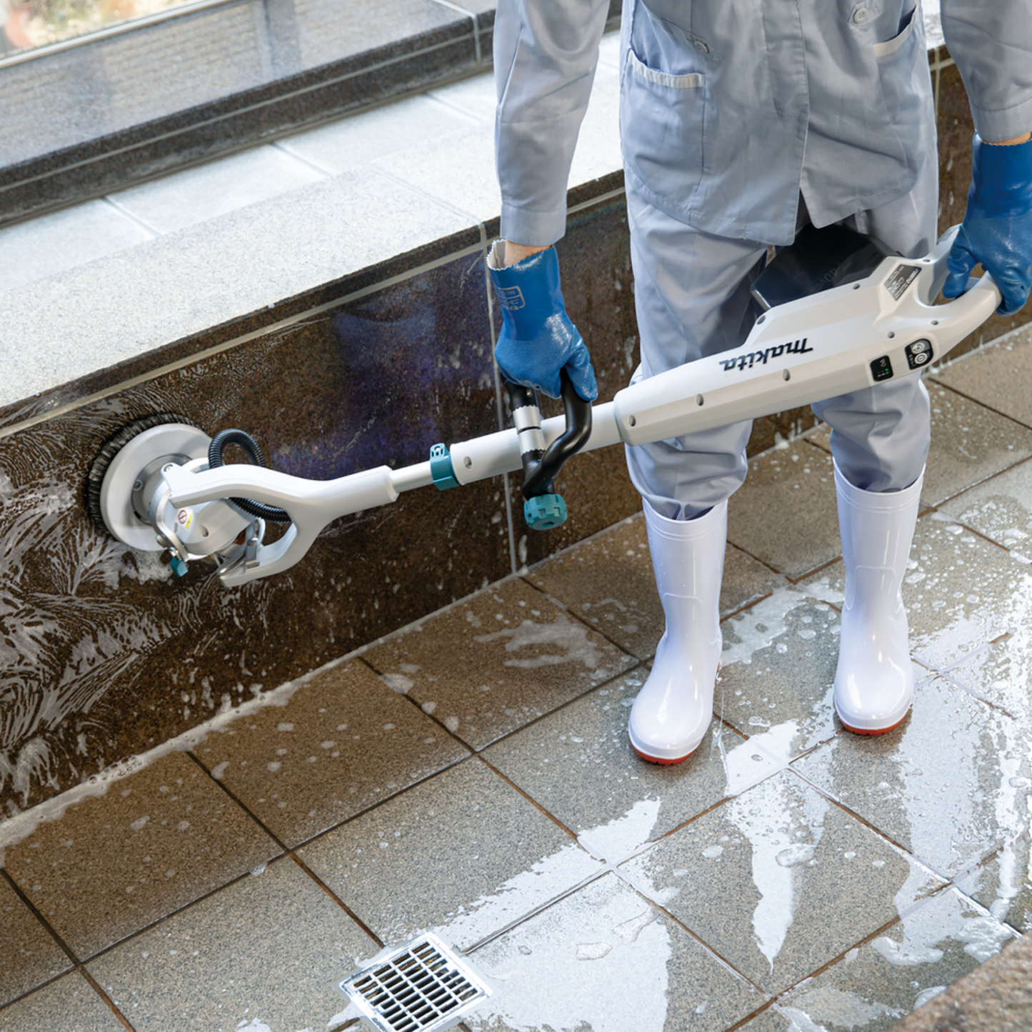 Person cleaning a tiled floor with a scrubber