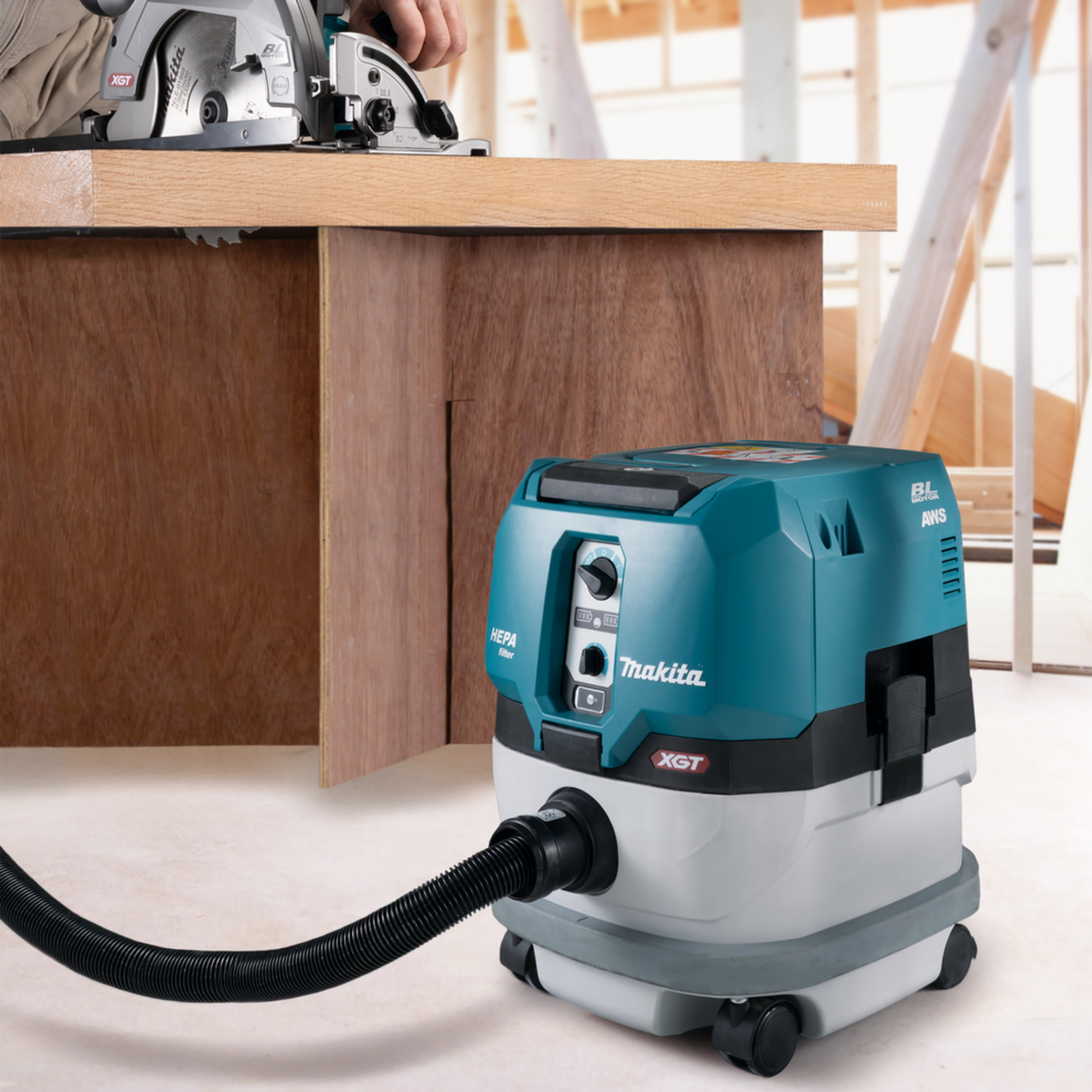 Makita vacuum cleaner on a workshop floor with a workbench and circular saw in the background.