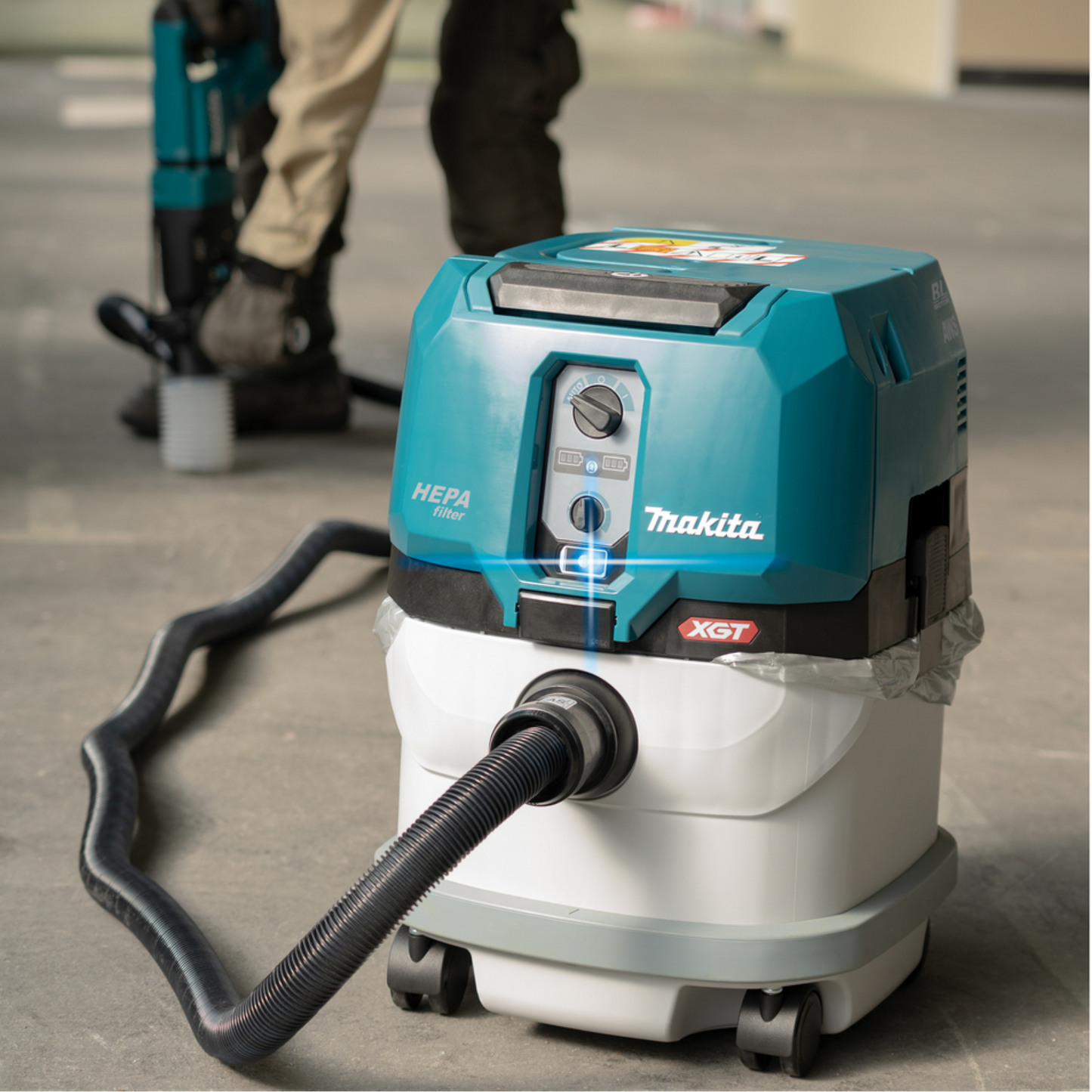 Makita vacuum cleaner on a concrete floor with a person in the background.