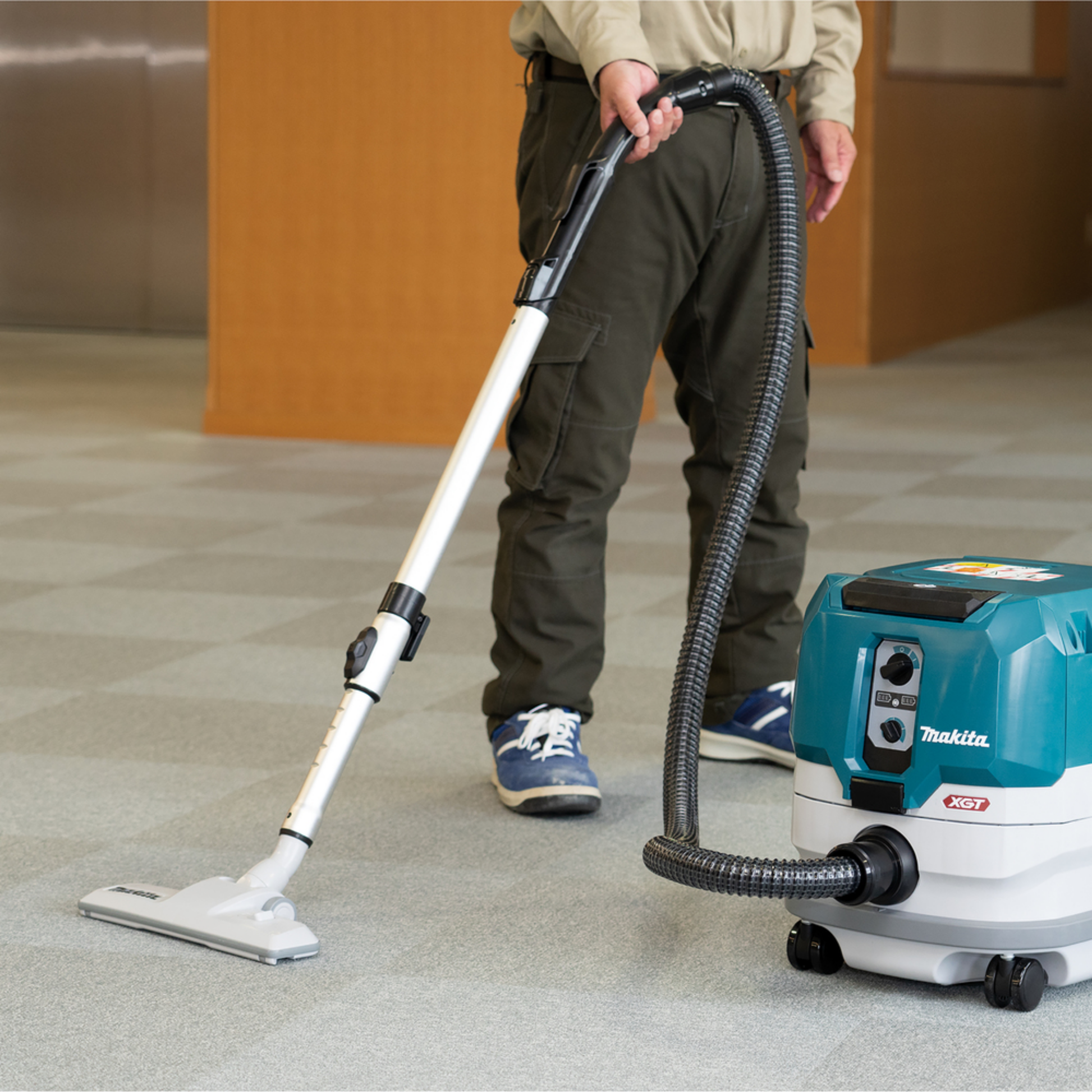 Person using a Makita vacuum cleaner on a carpeted floor.