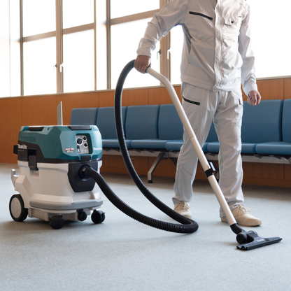 Person using a commercial vacuum cleaner in a room with blue seats.