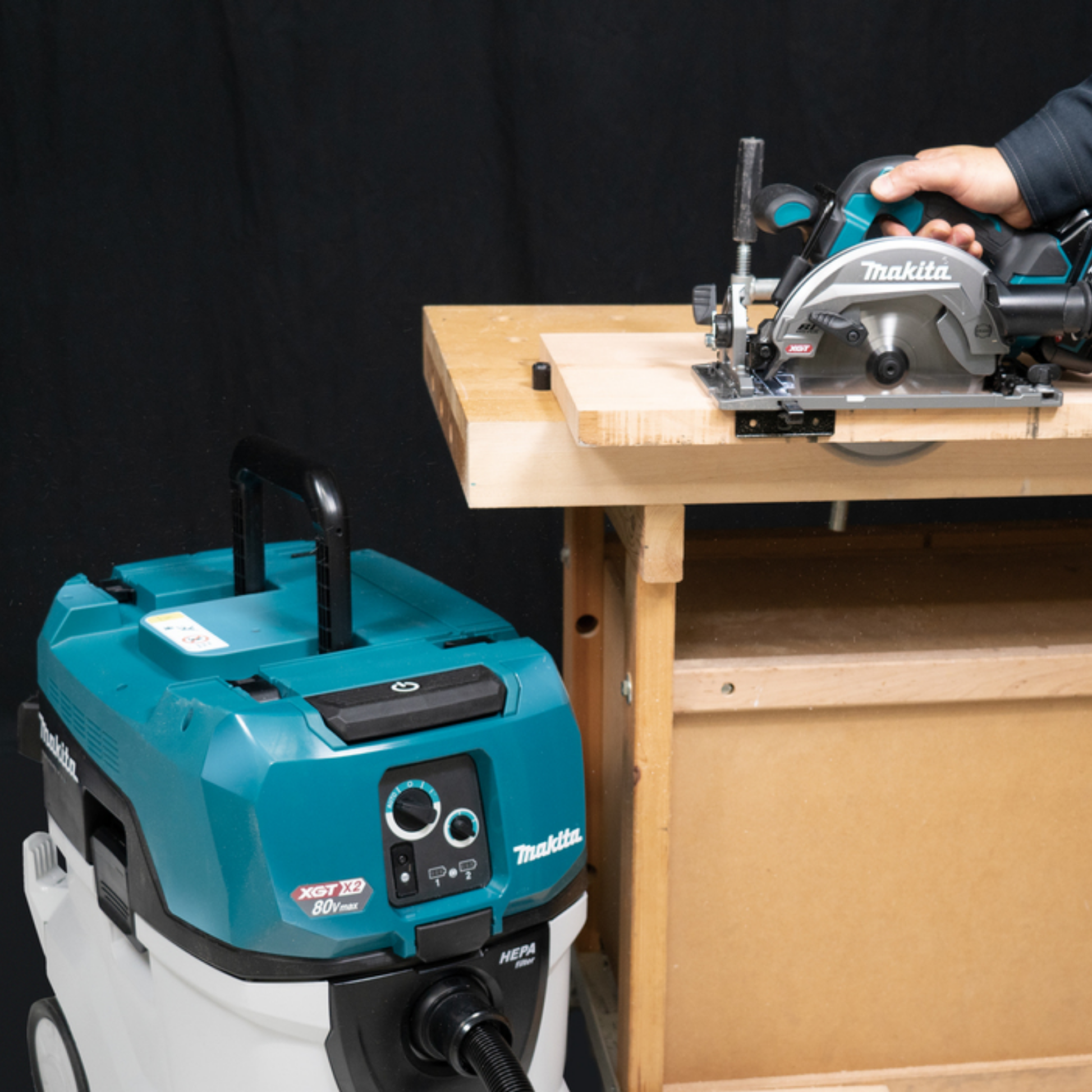 Makita circular saw and vacuum cleaner on a workbench with a black background
