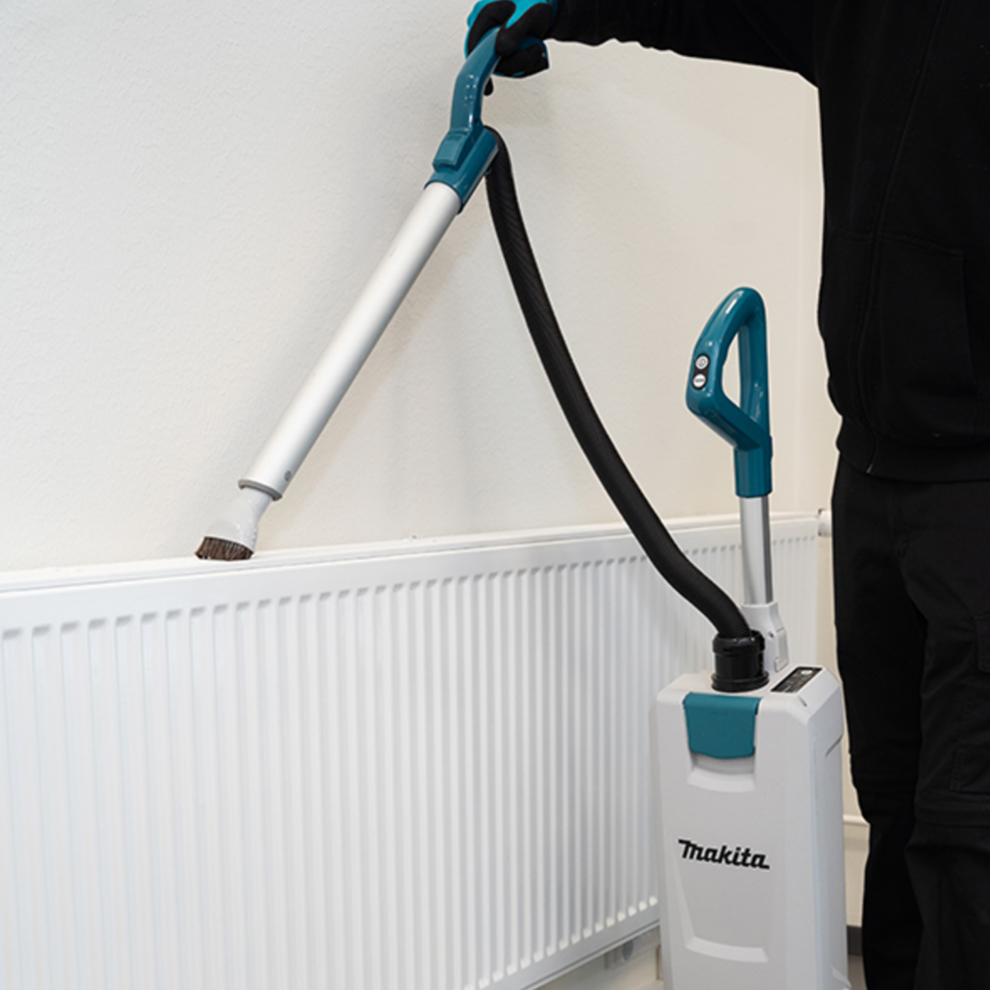Person using a Makita vacuum cleaner to clean a radiator.
