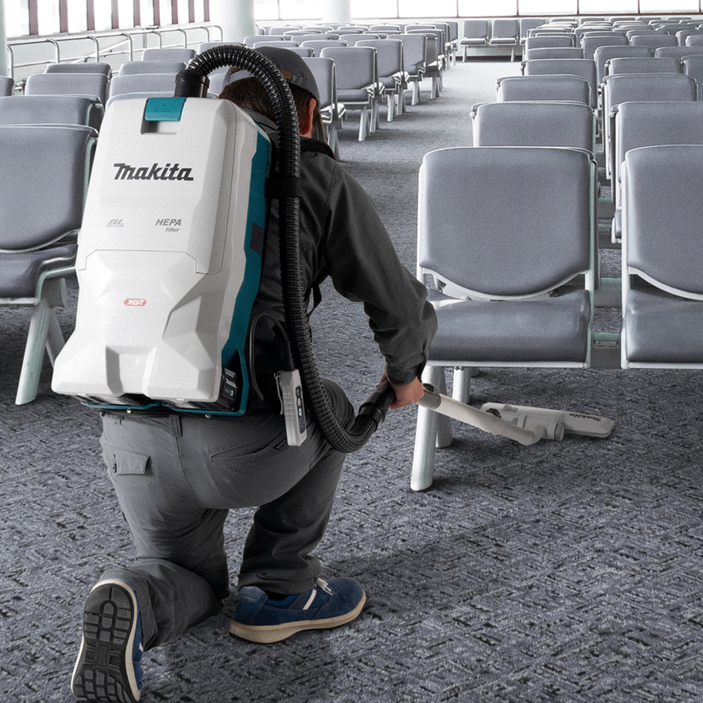 Person using a Makita backpack vacuum cleaner in an airport terminal.