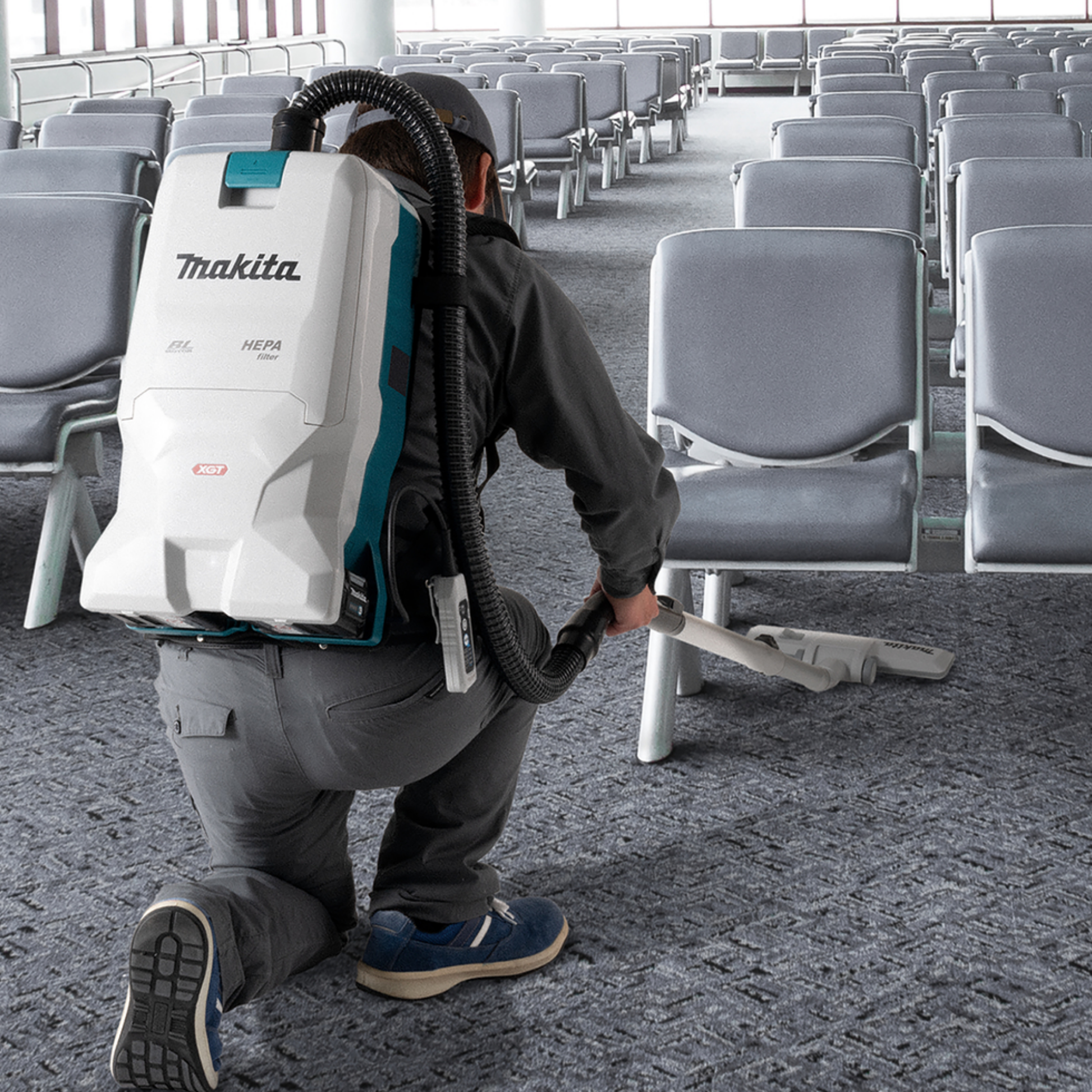 Person using a Makita backpack vacuum cleaner in an airport terminal.