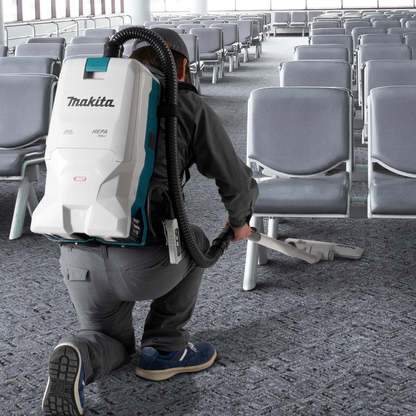 Person using a Makita backpack vacuum cleaner in an airport terminal.