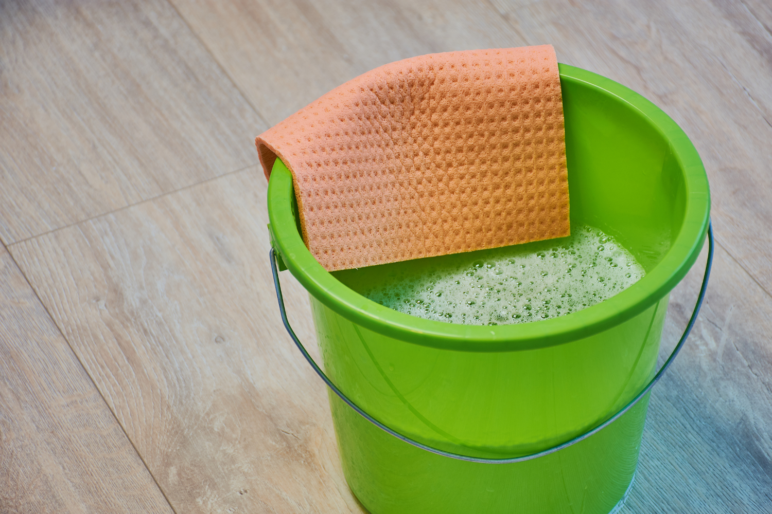 Green bucket with a sponge and cleaning solution on a wooden floor